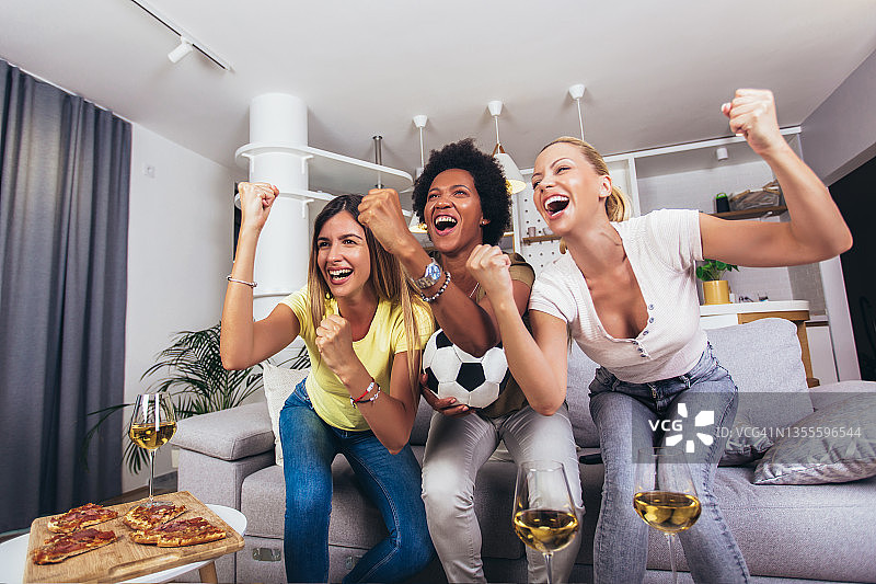 一群兴高采烈的女性朋友在家里观看足球比赛，庆祝胜利。图片素材