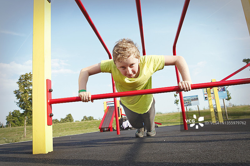 一个小男孩在户外健身房里做俯卧撑图片素材