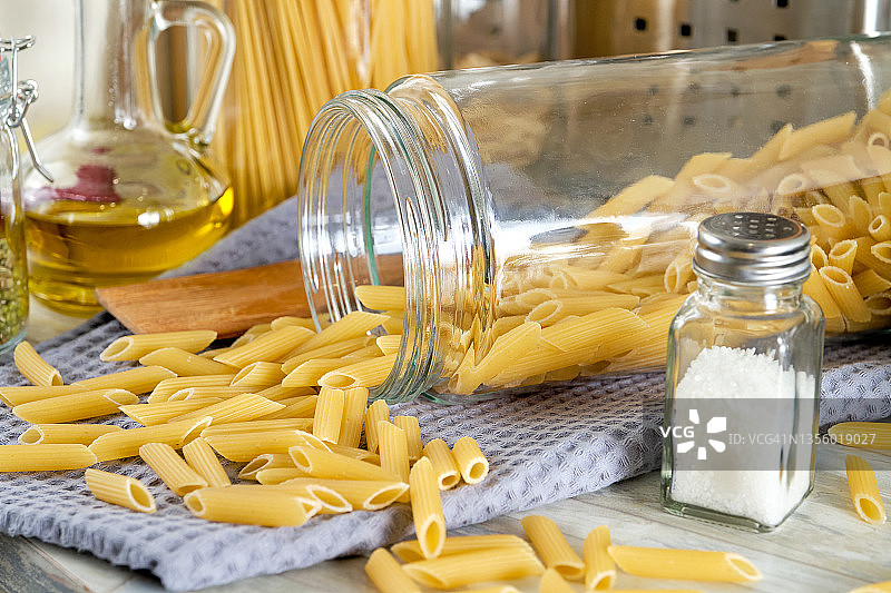 在家里用奶油酱和罗勒做意大利面。选择的通心粉。生的意大利通心粉放在玻璃罐里，放在厨房的桌子上。素食。按部就班，自己动手。步骤1。图片素材