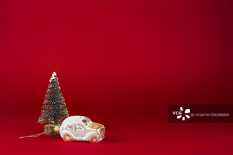 圣诞贺卡。白色的复古汽车旁边有一棵覆盖着雪的圣诞树，背景是红色。图片素材