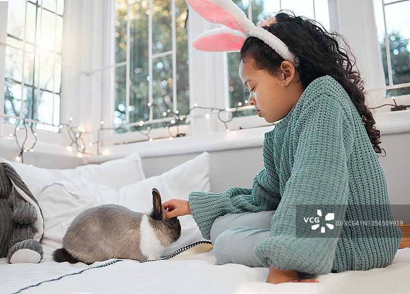 一个可爱的小女孩坐在床上，和家里的宠物兔子亲密接触图片素材