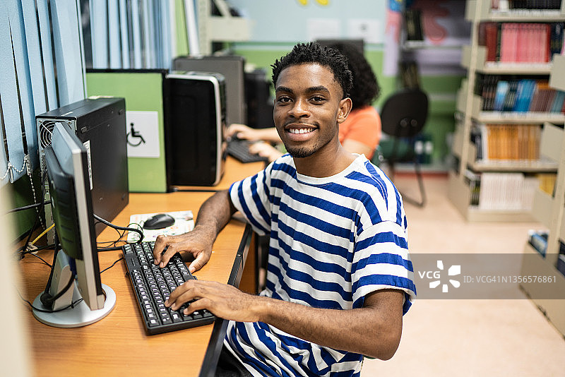 一个快乐的年轻人在图书馆使用电脑的肖像图片素材