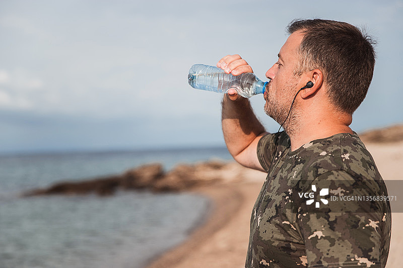 戴着耳机的成年人在沙滩上跑步时喝水图片素材