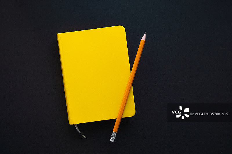 黄色的记事本和一支铅笔放在黑色的背景上。图片素材