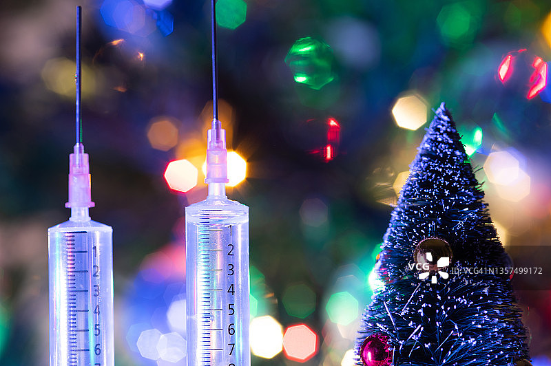 两个带疫苗的注射器的特写。圣诞彩灯靠近它。图片素材