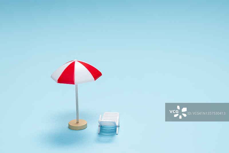 旅行的概念。太阳躺椅，蓝色背景下的红色雨伞。图片素材