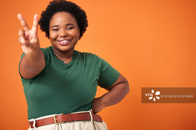 一个美丽的年轻女子站在橙色背景下，打出和平的手势图片素材