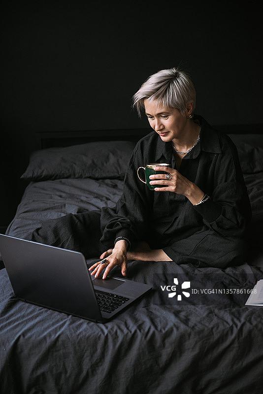 女性在家里用笔记本电脑工作，喝着咖啡，室内是黑色的图片素材