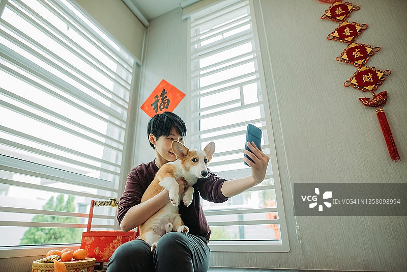 在中国新年期间，亚洲华人微笑的女性坐在客厅和她的狗自拍图片素材