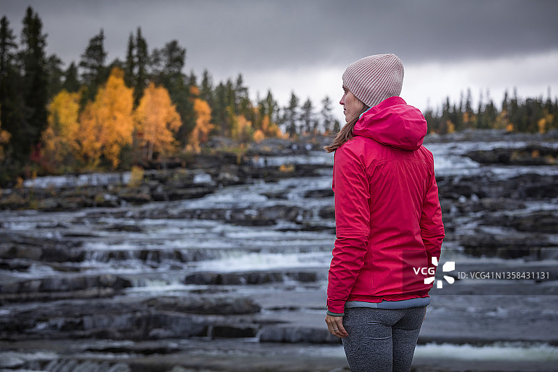秋天，瑞典拉普兰荒野之路的特拉普斯特福森瀑布旁的一名女子图片素材