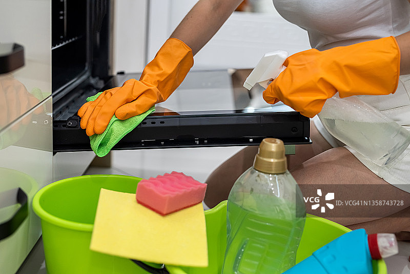 妇女用手套和一瓶洗涤剂清洁厨房烤箱图片素材