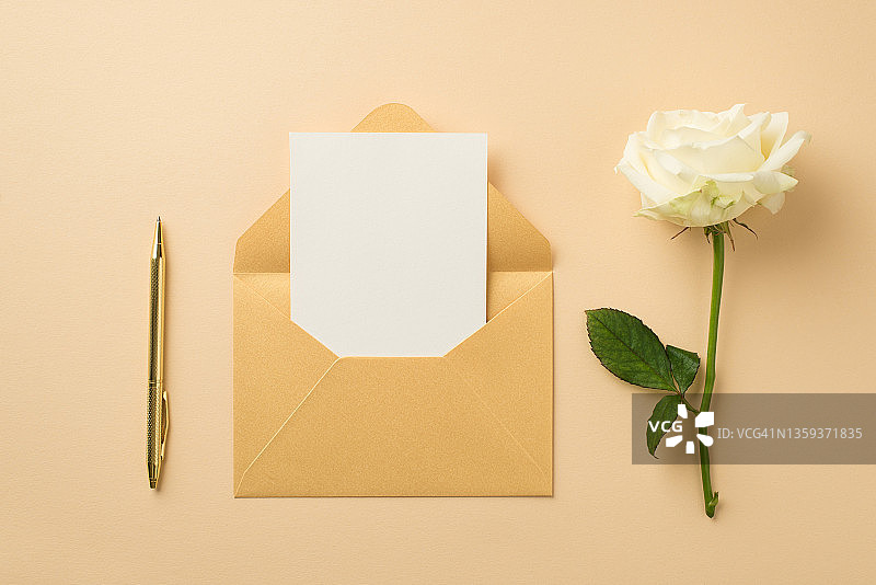 俯视图照片的秩序组成打开柔和的黄色信封与卡片金笔和白玫瑰在孤立的米色背景与空白的空间图片素材