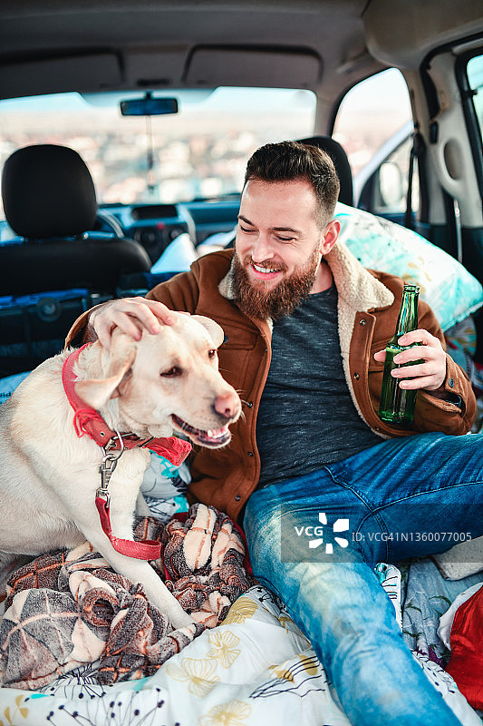 大胡子男人在小货车后面喝啤酒，抚摸狗图片素材