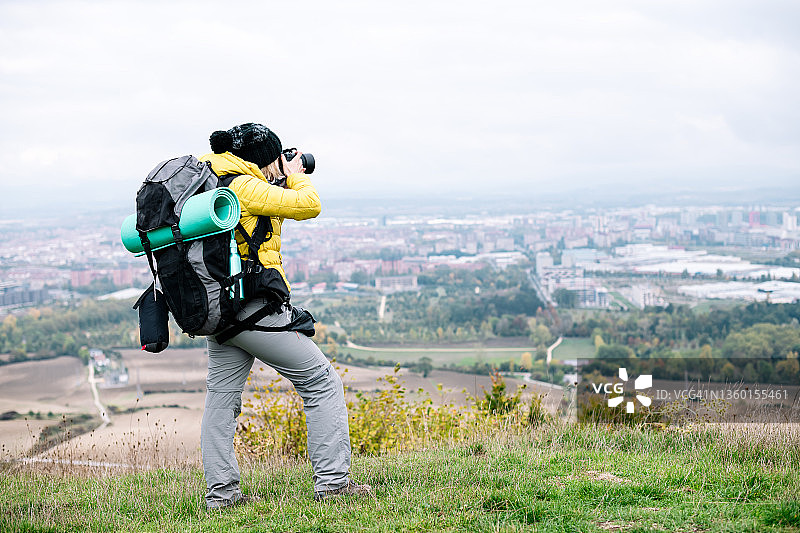 一个数字游牧民背着背包站在山顶上，用她的专业相机拍摄这座城市图片素材