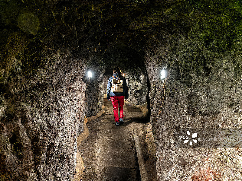 一个女人走在穿越山脉的岩石之间的行人隧道里。图片素材