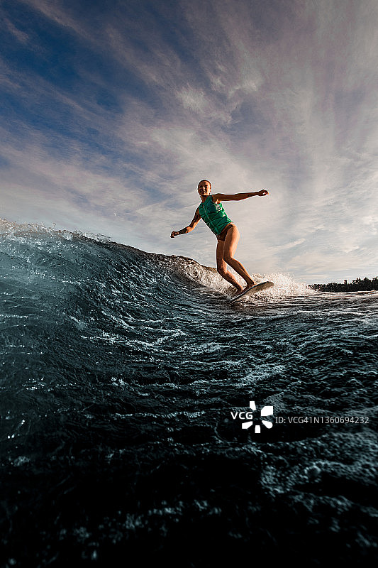 女尾浪冲浪者精力充沛地骑在尾浪板上，顺着河水的波浪冲下蓝天。图片素材