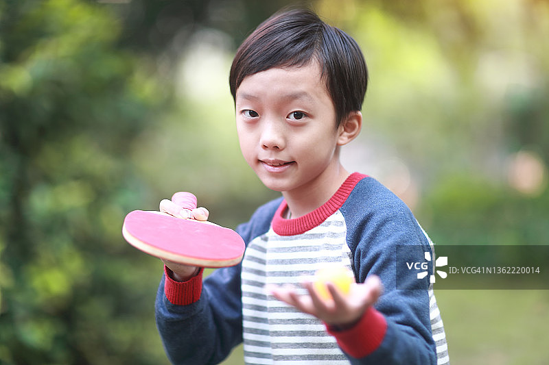 微笑的男孩在花园里打乒乓球图片素材