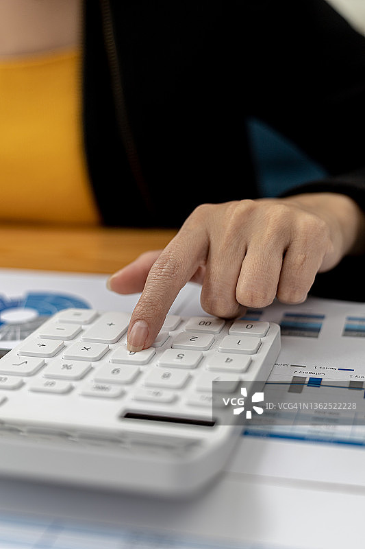 一个女商人使用白色计算器的特写镜头，一个金融商人正在检查公司财务文件上的数字数据，她使用计算器来验证数字的准确性。图片素材