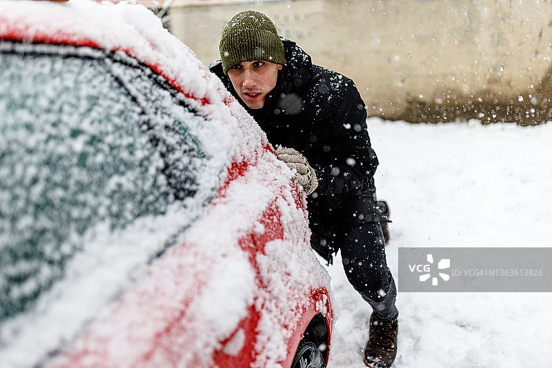 一名男子推着一辆陷在雪中的汽车。图片素材