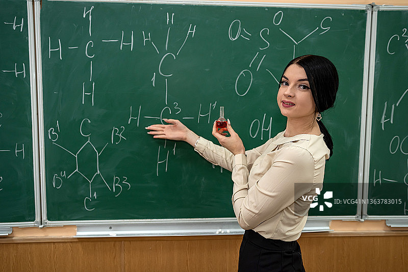 年轻漂亮的老师上化学课，站在黑板旁边拿着化学公式图片素材
