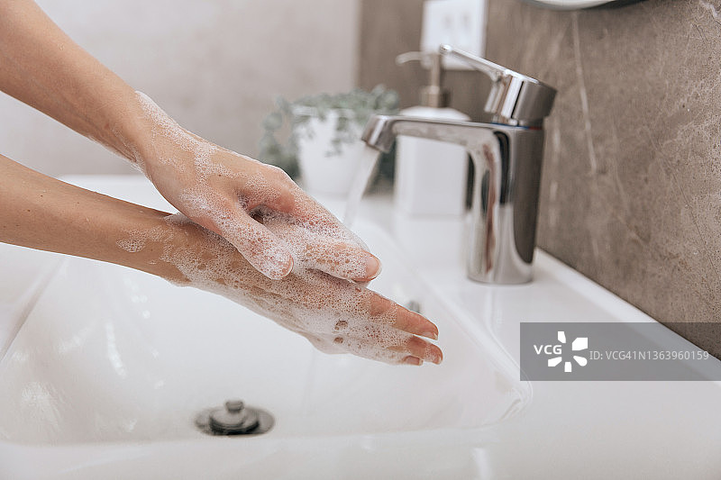 在水龙头下洗手。手部卫生概念细节。用肥皂洗手以预防冠状病毒的传播，防止冠状病毒在公共卫生间或公共卫生间的卫生传播图片素材