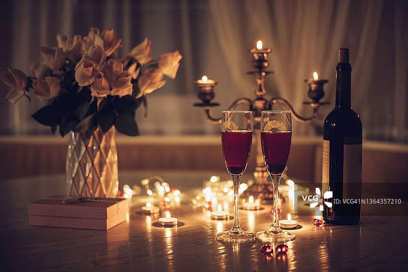 烛光日期。桌上摆着酒杯、蜡烛、玫瑰花束和礼盒。晚上在家浪漫的烛光晚餐图片素材