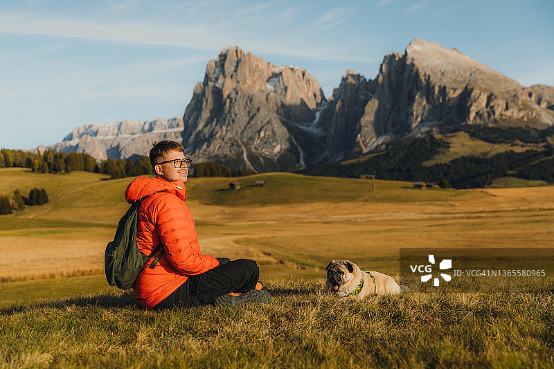 男性旅行者和他的狗在阿尔卑斯山的白云石山脉凝视日落的后视图图片素材