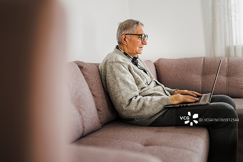 老人坐在沙发上用笔记本电脑在家图片素材