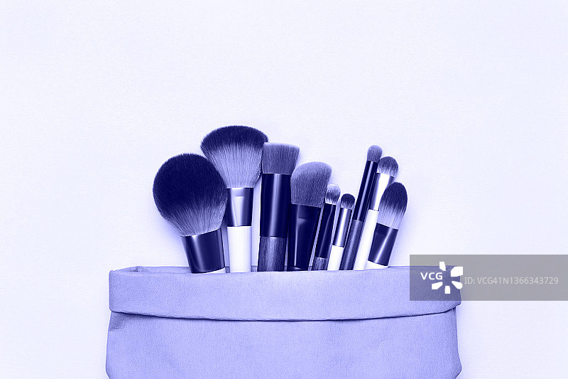 设置不同的软刷子化妆应用在白色背景的紫色纸袋。化妆品背景在平面布局风格与复制空间。极具2022年的色彩图片素材
