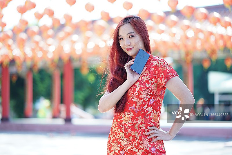 快乐的年轻亚洲妇女穿着传统旗袍旗袍，展示手机。中国新年概念图片素材