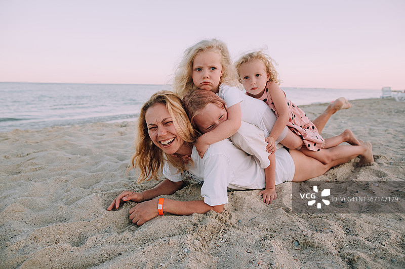 年轻的金发女人母亲和她的3个女儿在酒店的海滩上玩在日落在夏天的一天。全家人都躺在一起。图片素材