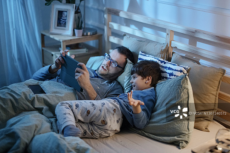父亲和儿子在深夜用数码平板电脑读睡前故事图片素材