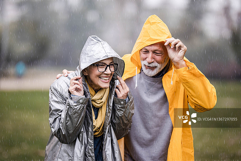 在公园里的雨中穿着雨衣的幸福成熟的夫妇。图片素材