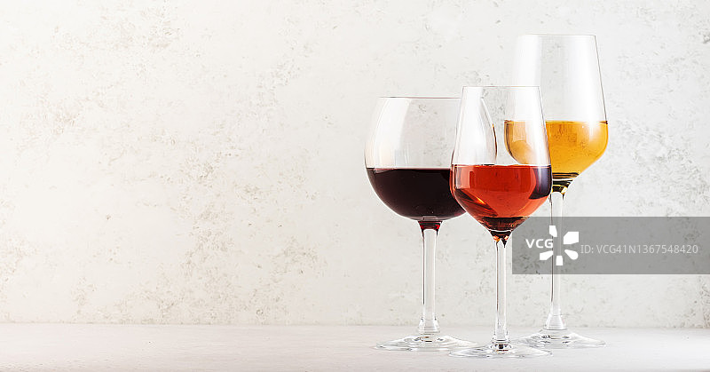 红、玫瑰和白葡萄酒酒杯设置在灰色的桌子背景上。品酒。强光和阴影图片素材