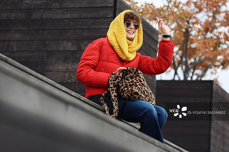 年轻自信的女子，戴着黄色针织围巾，坐在木街露台上图片素材