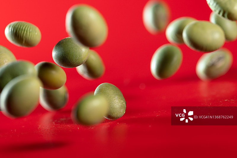 绿色的大豆在半空中飞在红色的背景中图片素材