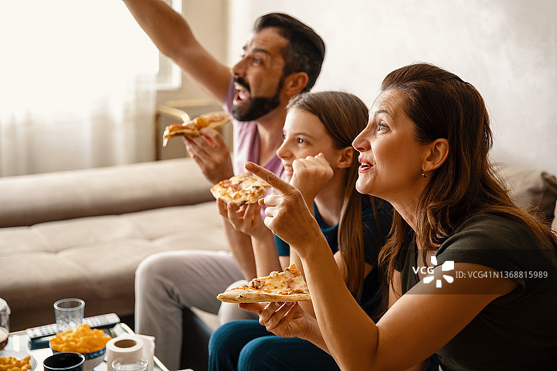 一家人吃着披萨，在电视上看最喜欢的体育节目图片素材