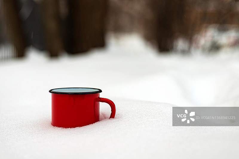 红色金属杯，装着热饮，站在雪林里。冬季旅游野餐概念。特写镜头。图片素材