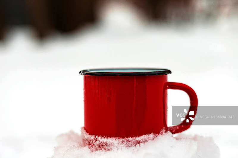 红色金属杯，装着热饮，站在雪林里。冬季旅游野餐概念。特写镜头。图片素材