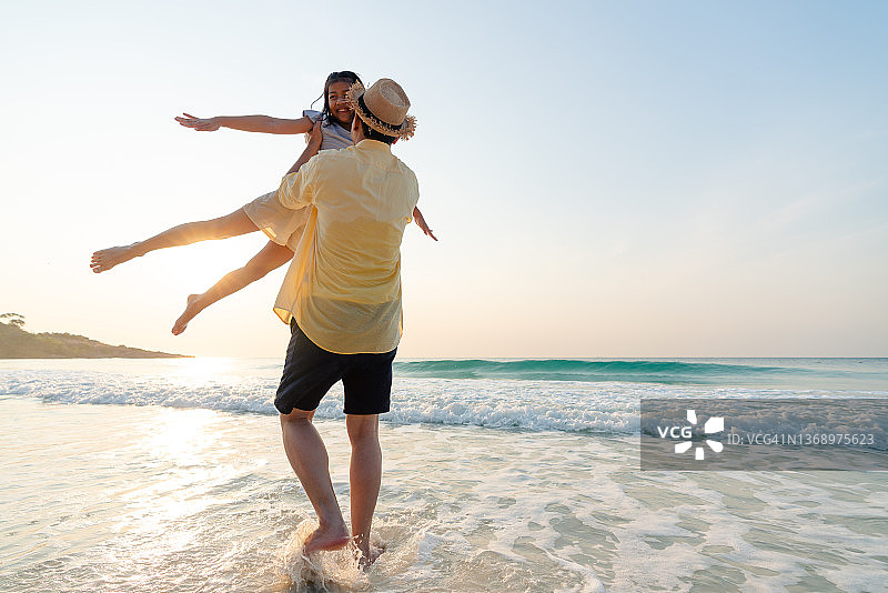快乐的爸爸抱着会飞的女儿在海滩上享受假期图片素材