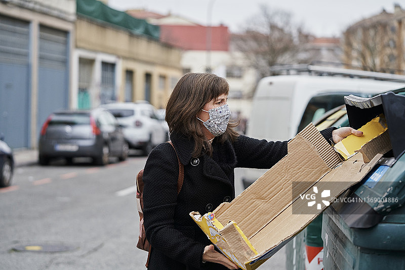 妇女在街上把垃圾扔进回收箱。图片素材
