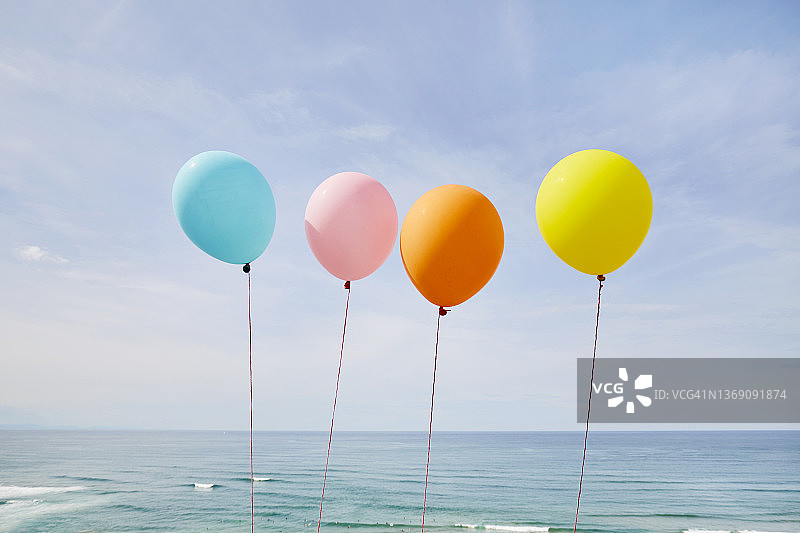 五颜六色的气球在大海和蓝天的映衬下排成一行图片素材