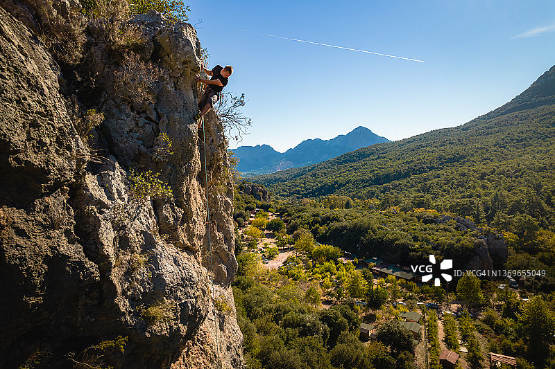 攀登者攀爬郁郁葱葱的山谷上陡峭的岩壁图片素材