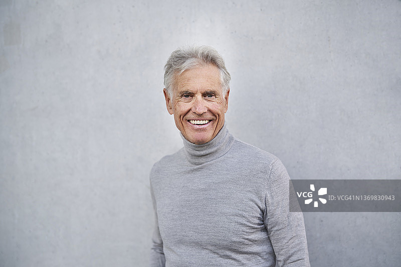 一位面带微笑的老人站在灰色的墙前图片素材