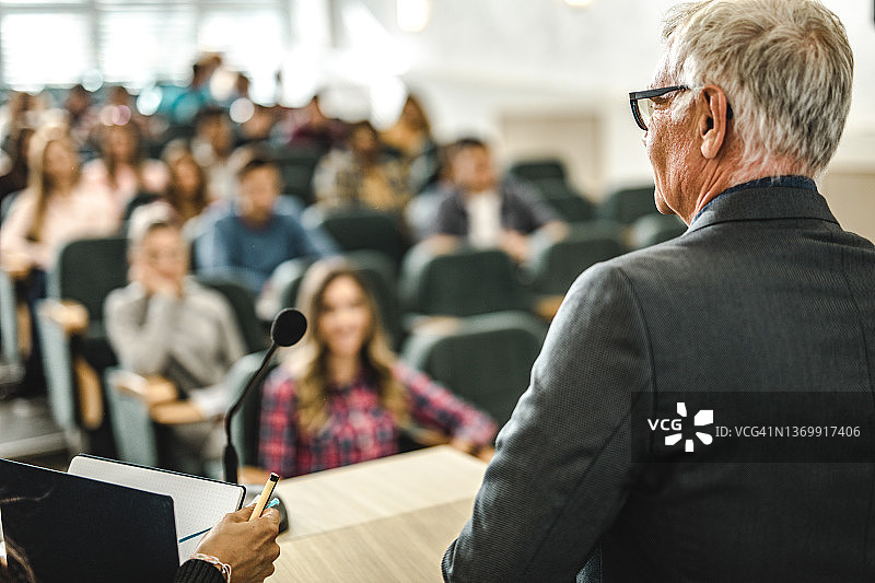 一个成熟的教授在演讲厅里教他的学生的后视图。图片素材