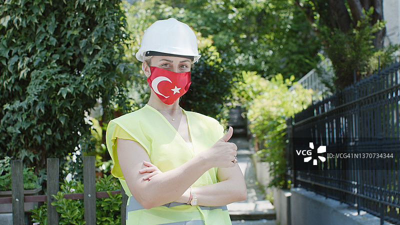 女工程师的肖像微笑着对着镜头，头盔，防护背心和防护面具与土耳其国旗。图片素材