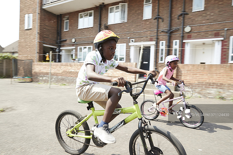 兄弟姐妹在阳光明媚的社区里骑自行车图片素材