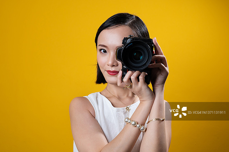 年轻美丽的亚洲女子拿着数码相机，戴着金戒指、耳环、项链和手镯等奢侈饰品图片素材