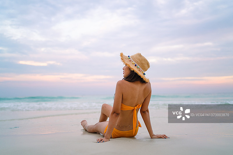 穿着黄色比基尼的亚洲妇女的肖像坐在沙滩上享受暑假图片素材