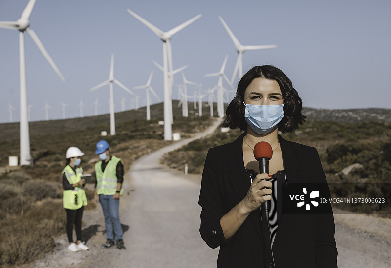 戴着口罩的女电视新闻记者在大流行期间报道可再生能源图片素材